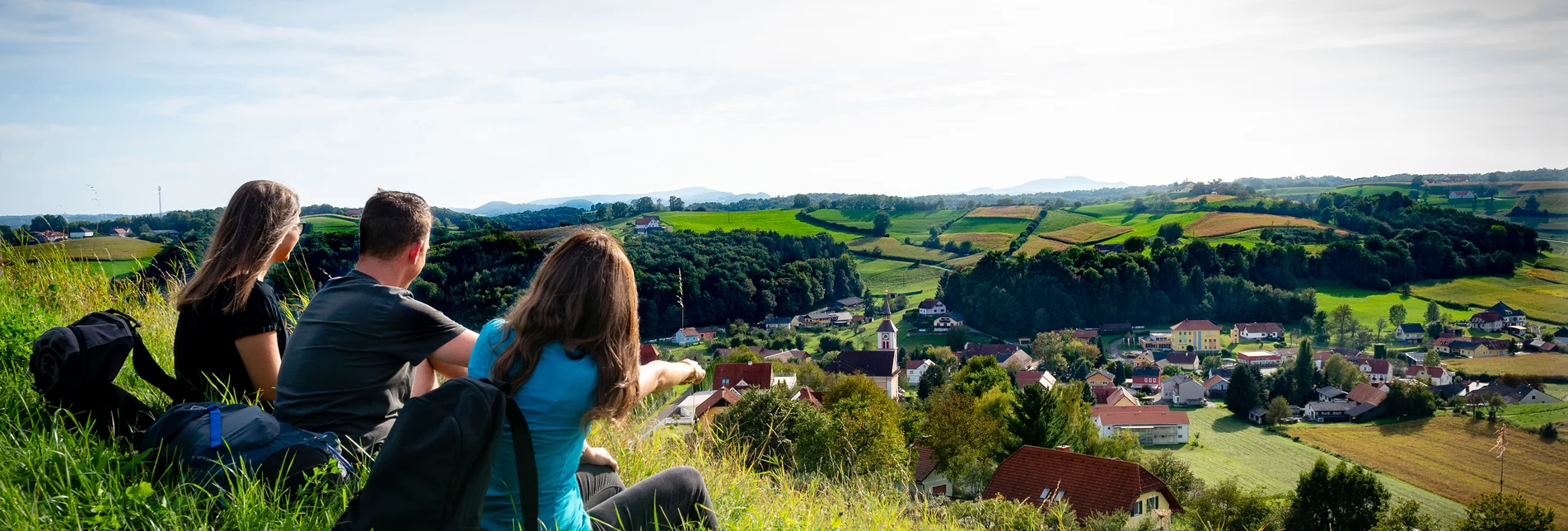 Zwei Frauen und ein Mann sitzen auf der grünen, saftigen Wiese und blicken auf Unterlamm im Thermen- & Vulkanland Steiermark
