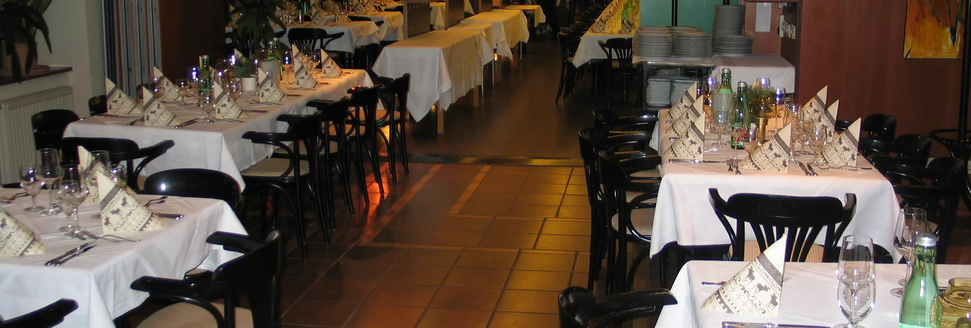Blick vom Seminarraum Richtung Cafe mocca im Restaurant Schicker mit gedeckten Tischen mit schwarzen Stühlen, einem Kleiderständer und Grünpflanzen