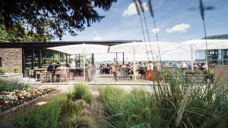 Gemütliche Terrasse mit Gästen, Sonnenschirmen und schöner Pflanzenlandschaft.