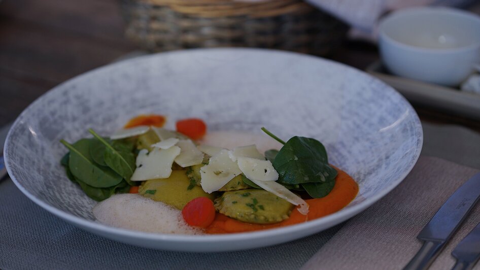 Ein raffinierter Teller mit Ravioli, Spinat, Tomaten und Parmesan.