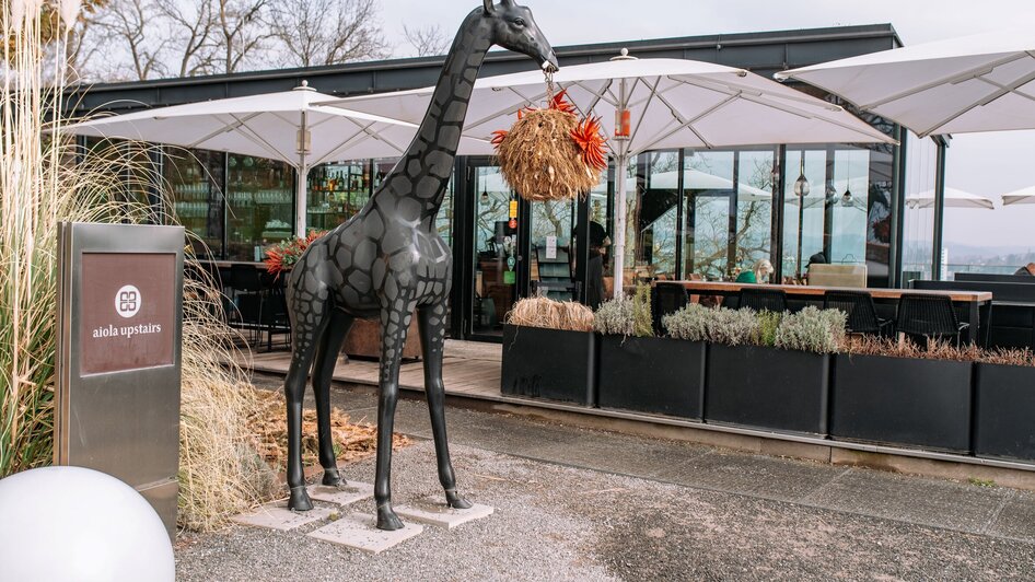 Eine stilisierte Giraffen-Skulptur vor dem aiola upstairs Restaurant.