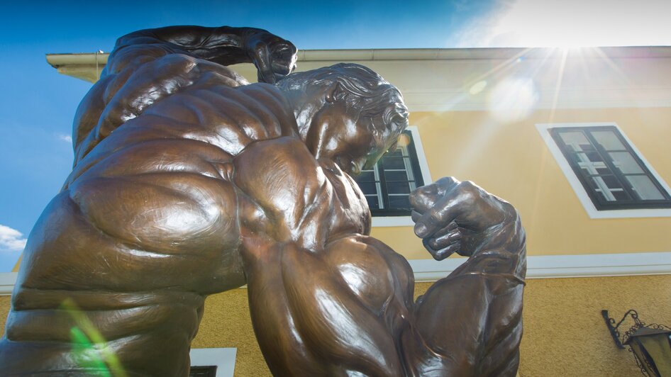 Nahaufnahme einer beeindruckenden Bronzestatue des Bodybuilders Arnold Schwarzenegger mit muskulösem Oberkörper. | © Region Graz - Harry Schiffer