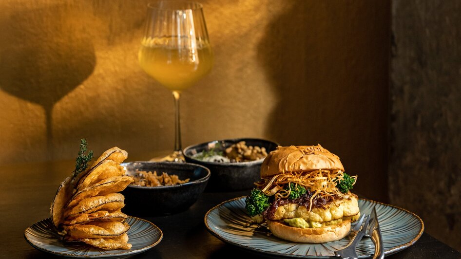 Ein leckerer Burger mit Beilagen und Wein in einem Restaurant. | © Lucija Novak