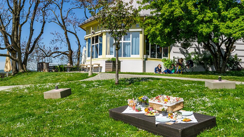 Eine sonnige Wiese mit einem Picknickkorb vor einem Café in Graz.