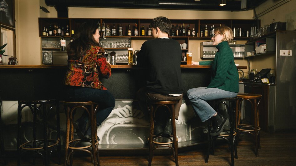 Drei Personen sitzen an einer Bar in einem gemütlichen Lokal. | © G. Obetzhofer