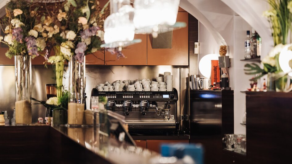 Gemütliches Café mit Blumenarrangement und Espressomaschine. | © Ripix