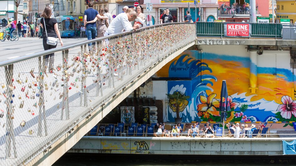 Überblick über die Mur und die bunten Graffitis in Graz, mit einer Brücke voller Liebesschlösser. | © Graz Tourismus - Harry Schiffer