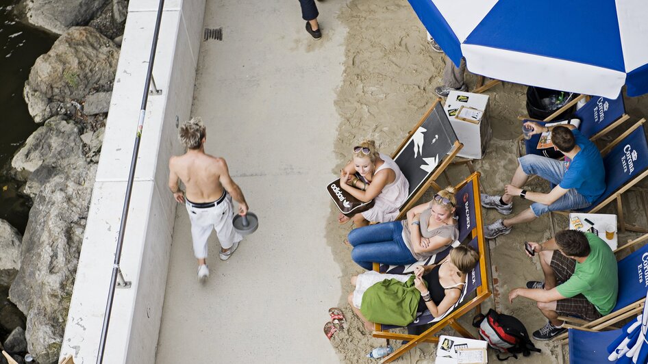 Menschen genießen die Sonne am Murufer, während andere vorbeigehen. | © Graz Tourismus - Toni Muhr
