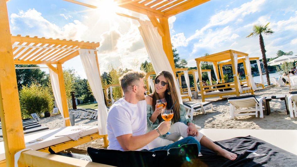 Ein Paar genießt Cocktails in einer Strandlounge mit Sonnenschein. | © Region Graz - Mias Photoart