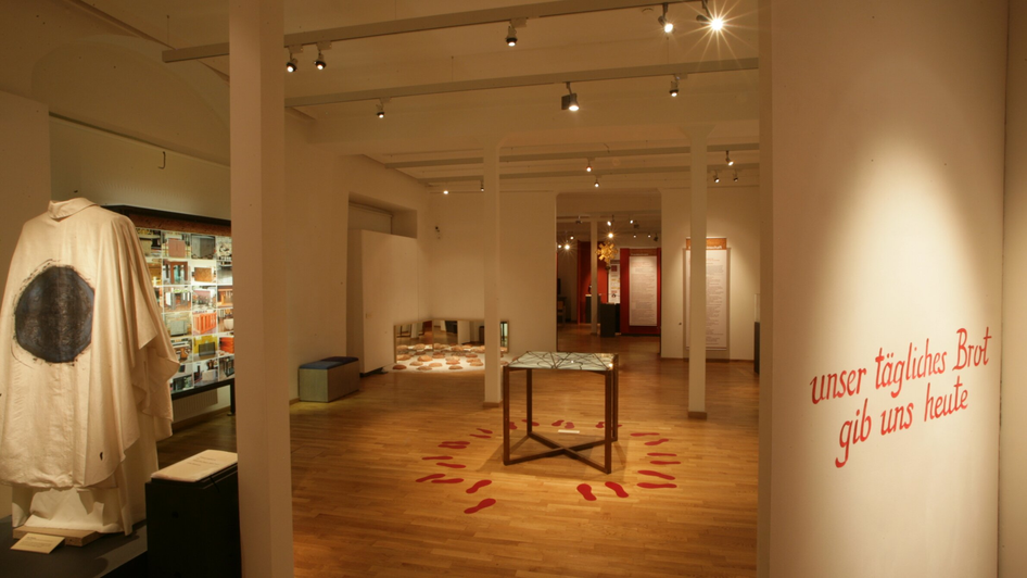 Innenansicht einer Ausstellung mit Fußspuren und dem Text: 'unser tägl. Brot gib uns heute'.