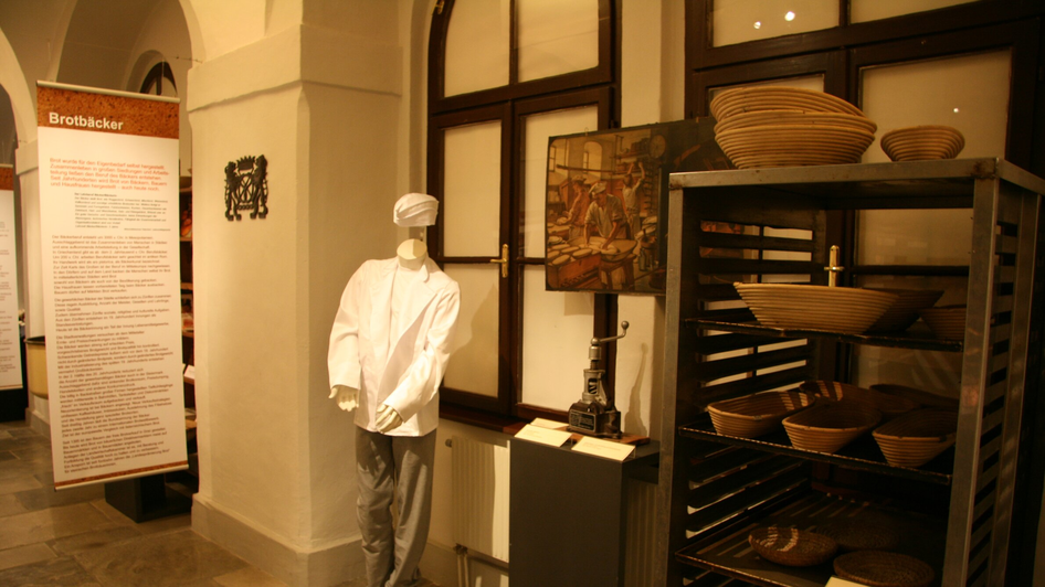 Eine Ausstellung mit einer Schaufensterpuppe in Bäckerkleidung, historischen Backwerkzeugen und Brotformen.