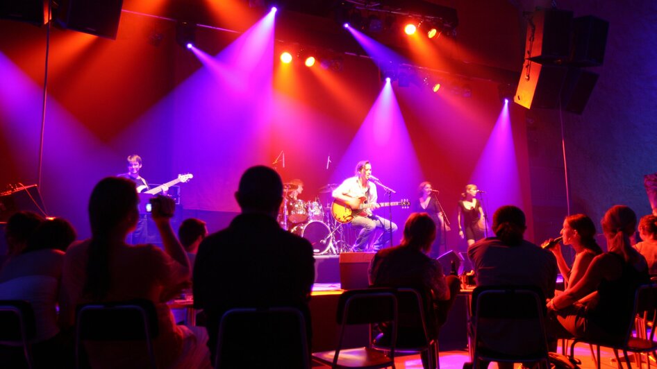Eine Band spielt live auf der Bühne im Dom im Berg mit bunten Lichtern.