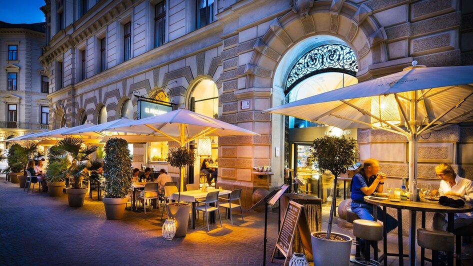 Gemütlicher Gastgarten des Restaurants "El Pescador im Rathaus" in Graz bei Dämmerung, Gäste genießen ihr Essen. | © El Pescador - Werner Krug