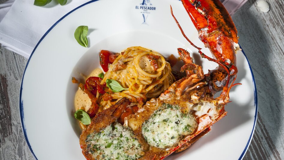 Hummer mit Pasta, Kräuterbutter und Beilagen auf einem Teller. | © El Pescador - Werner Krug