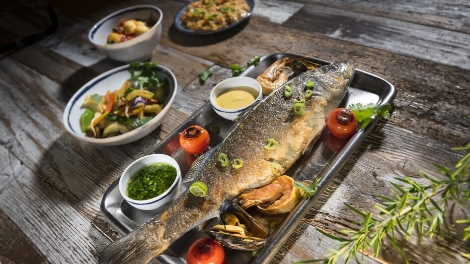 Ein gegrillter Fisch mit Garnelen und Saucen, serviert mit Beilagen. | © El Pescador