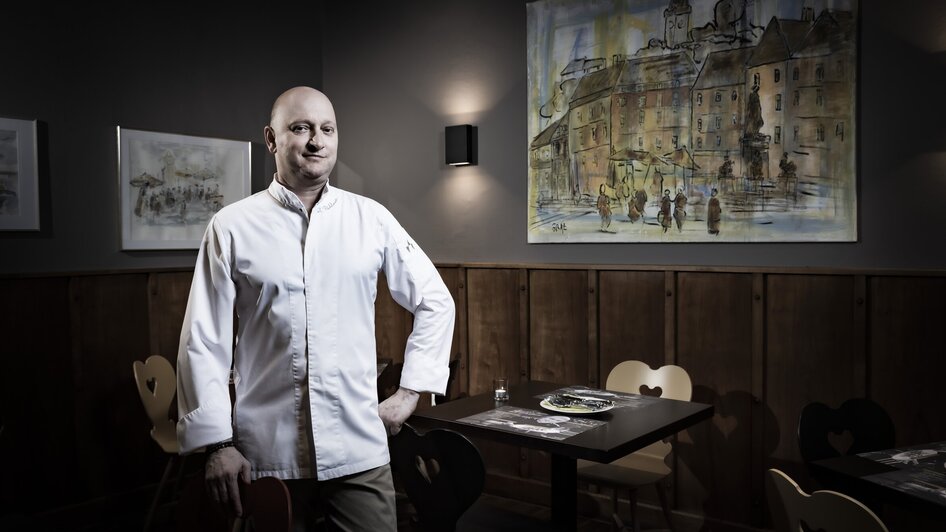 Ein Koch steht in einem Restaurant mit einem Gemälde im Hintergrund. | © Graz Tourismus - Werner Krug