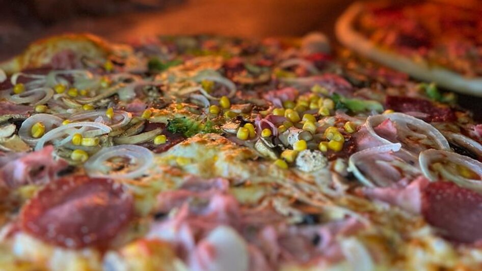 Leckere Pizza wird im Holzofen gebacken, mit Feuer im Hintergrund. | © Forno Antico