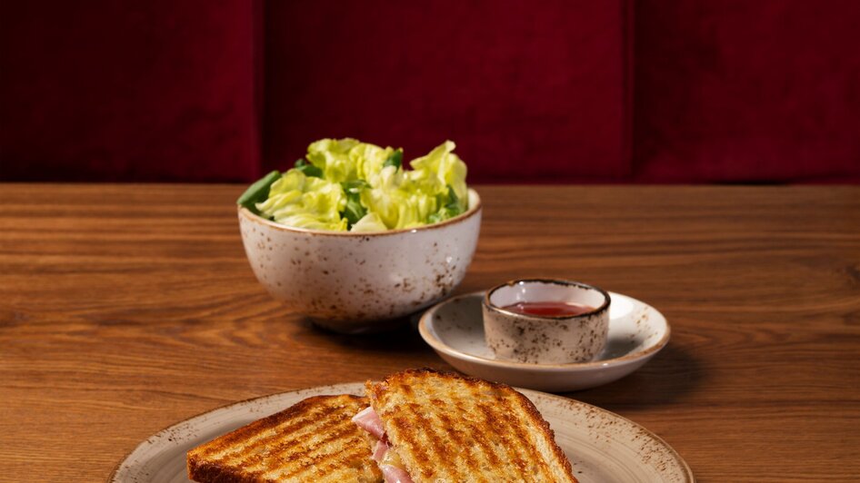 Gegrilltes Sandwich mit Salat und Dips auf einem Holztisch.
