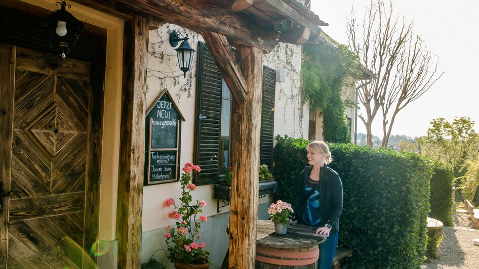 Eine Frau steht vor einem rustikalen Gebäude mit Blumen. | © Graz Tourismus - Mias Photoart