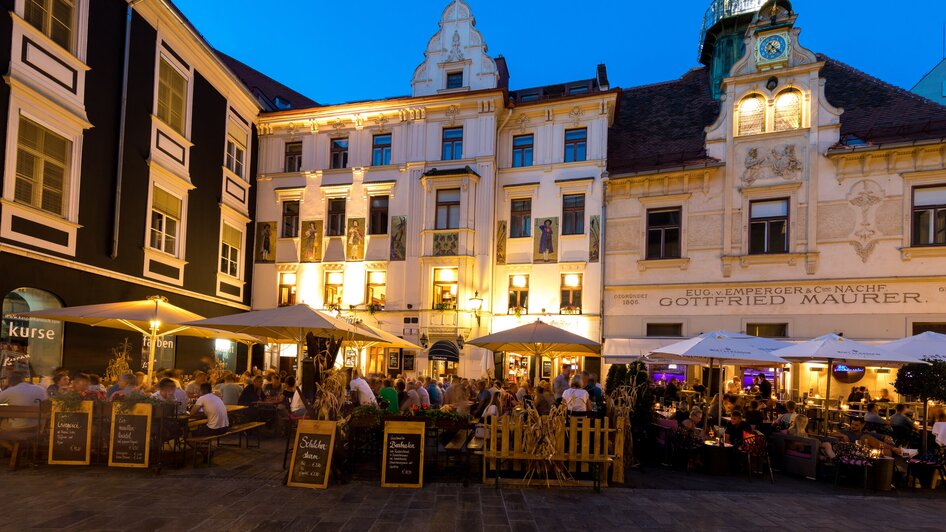 Belebter Glockenspielplatz mit Restaurants und beleuchtetem Glockenspiel. | © Graz Tourismus - Harry Schiffer