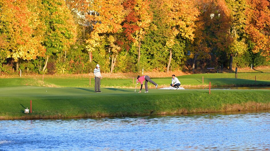Golfspieler auf einem Putting Green, umgeben von bunten Herbstbäumen.