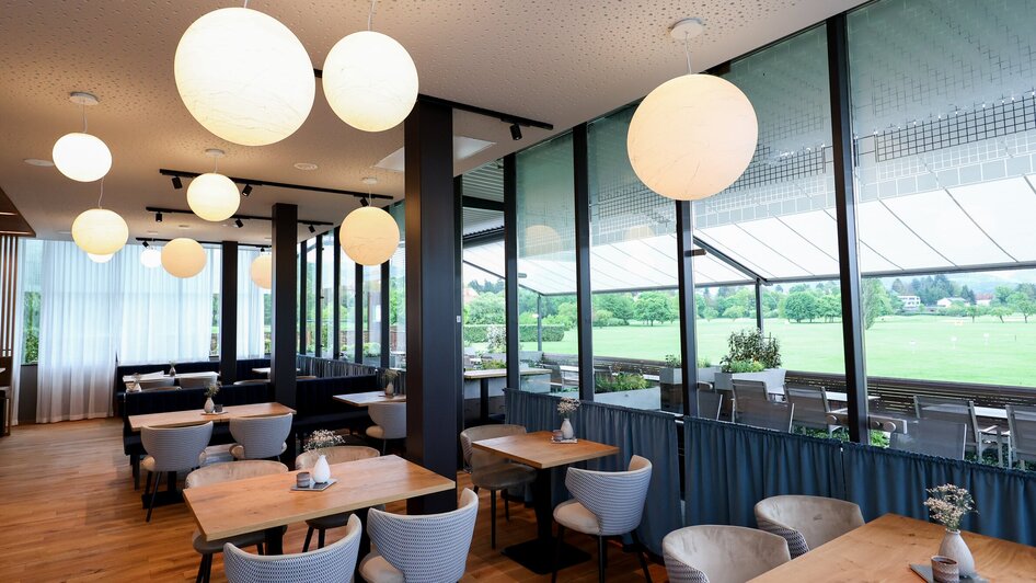 Moderne Innenansicht eines Restaurants mit runden Lampen und Blick auf den Golfplatz.