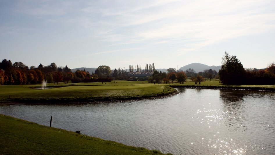 Ansicht des Golfzentrums Andritz mit Wasser und Bäumen im Herbst.