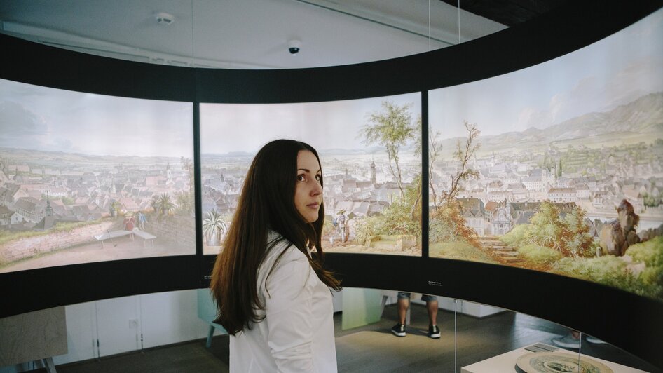 Eine Person steht vor Gemälden im Graz Museum Schlossberg. | © Sebastian Reiser