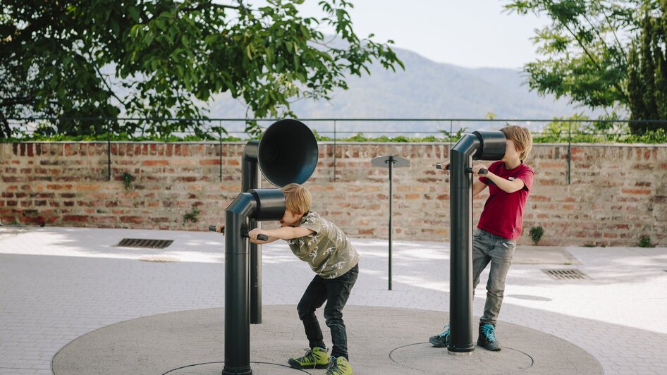 Zwei Jungen spielen an Klangskulpturen im Freien, begeistert von den Geräuschen. | © Sebastian Reiser