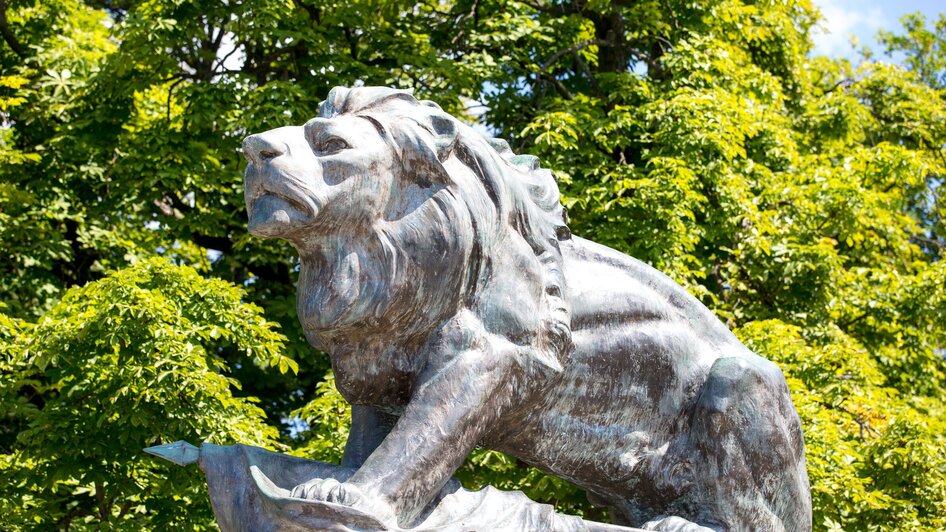 Bronze-Löwenskulptur auf dem Grazer Schlossberg vor grünen Bäumen. | © Graz Tourismus - Harry Schiffer