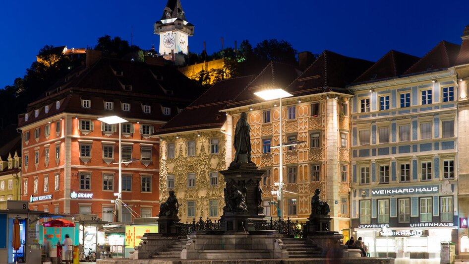 Beleuchteter Hauptplatz in Graz mit Grazer Uhrturm im Hintergrund.
