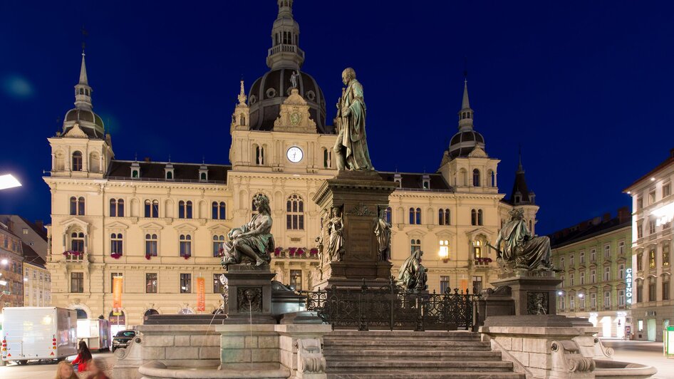 Abendliche Ansicht des Rathauses am Hauptplatz in Graz mit Statuen und historischem Hintergrund.