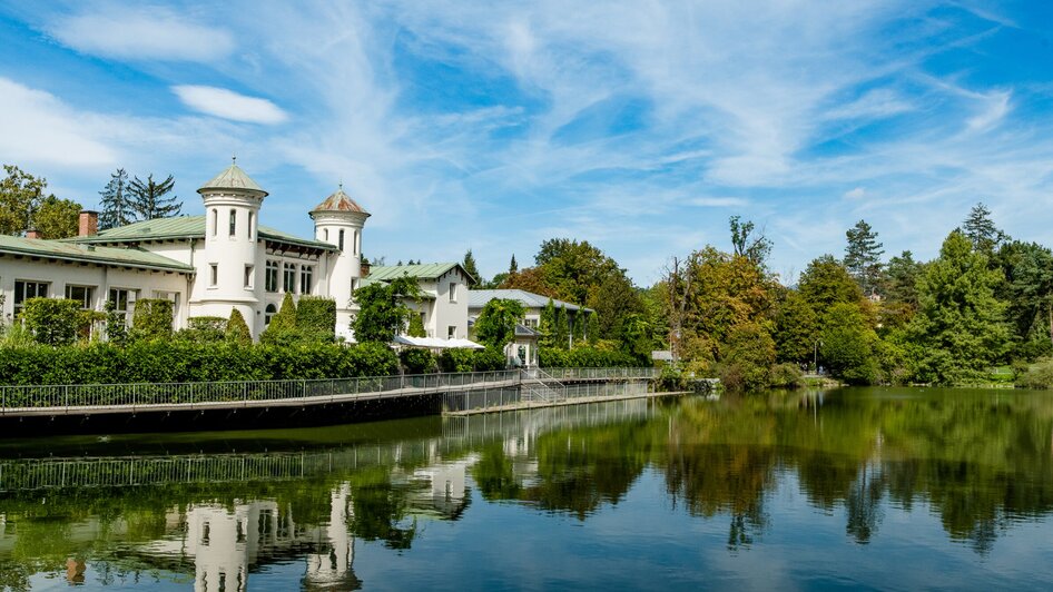 Ein malerisches Gebäude am Grazer Hilmteich spiegelt sich im Wasser.
