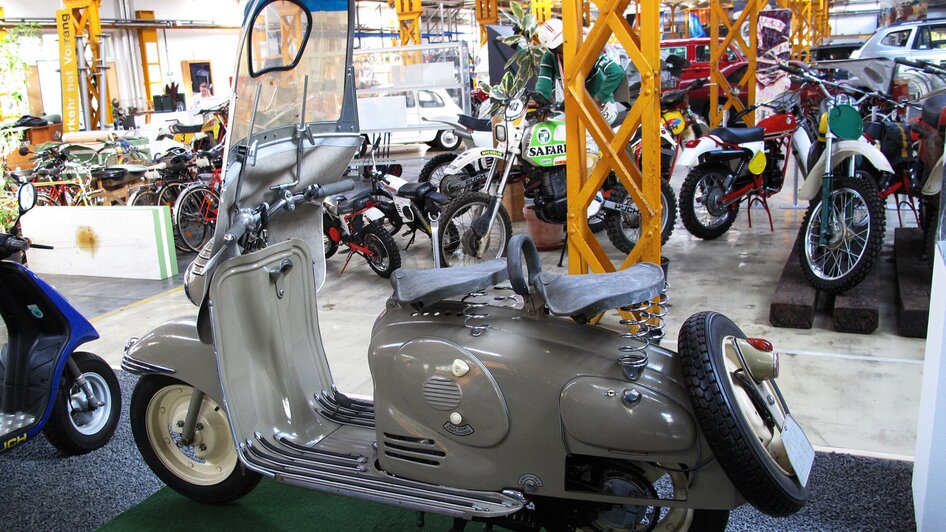 Eine Retro-Motorradskulptur in einem Museum, umgeben von anderen Fahrzeugen. | © Johann Puch Museum