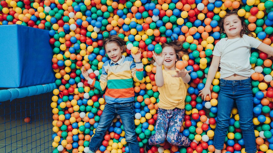 Drei fröhliche Kinder liegen in einem bunten Bällebad. | © Lex Karelly