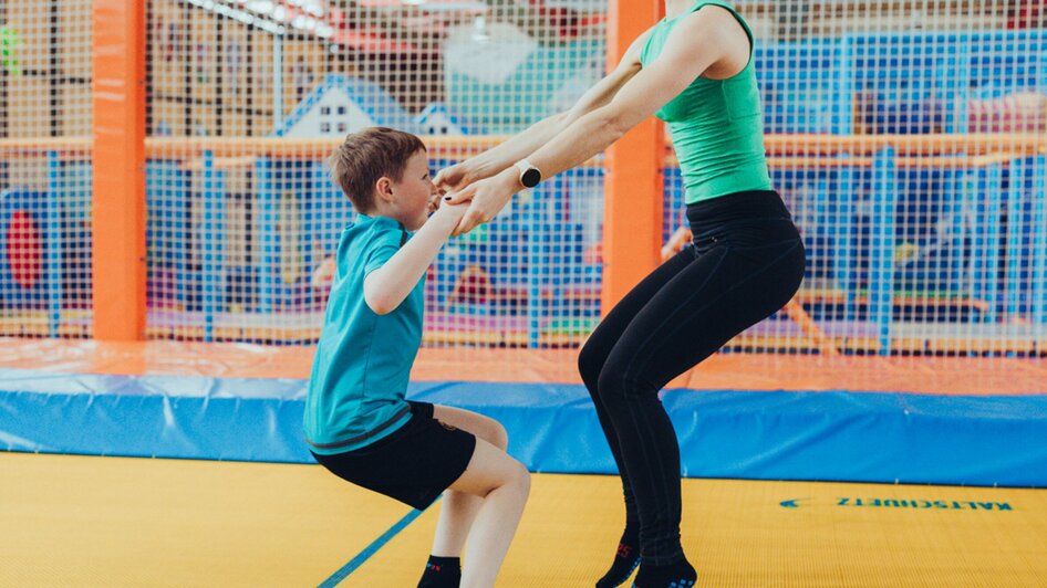 Eine Frau hilft einem Kind beim Springen auf einem Trampolin. | © Lex Karelly