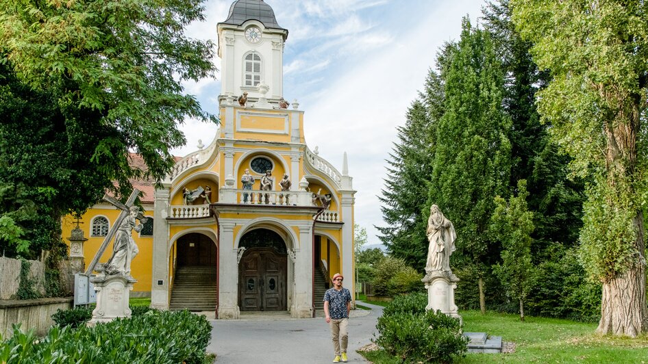 Mann vor der Kalvarienbergkirche in Graz mit Statuen im Garten.