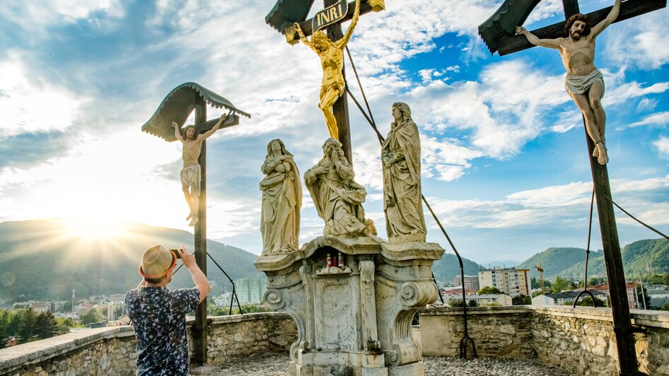 Besucher fotografiert Kreuzigungsszenen am Grazer Kalvarienberg mit Stadt im Hintergrund.
