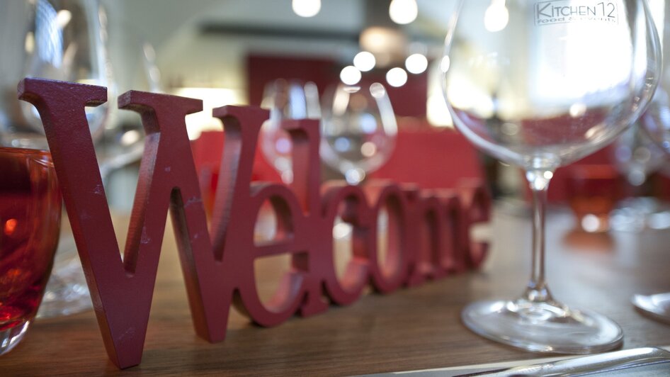 Gedeckter Tisch mit 'Welcome'-Schild und Weingläsern in einem Restaurant. | © kitchen 12 - Christian Jungwirth