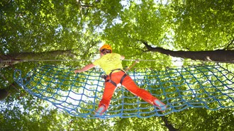 Person klettert in einem Kletterwald mit grüner Baumkulisse. | © WAP