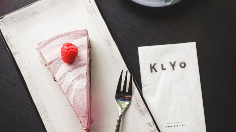 Ein Stück Himbeertorte mit einer Kaffeetasse im Restaurant KLYO.