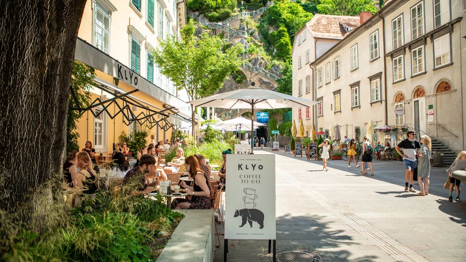 Gemütliches Restaurant am Schlossbergplatz in Graz mit Gästen und grüner Umgebung.