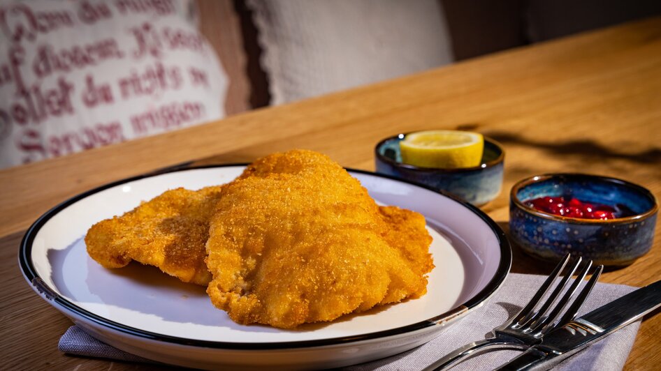 Panierte Schnitzel mit Zitrone und Preiselbeeren auf einem Teller mit Besteck. | © Kreuzwirt am Rosenberg in Graz