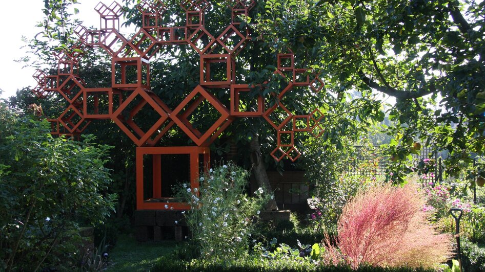 Ein kreativer Garten mit einem auffälligen, orangefarbenen Baumdesign aus geometrischen Formen.