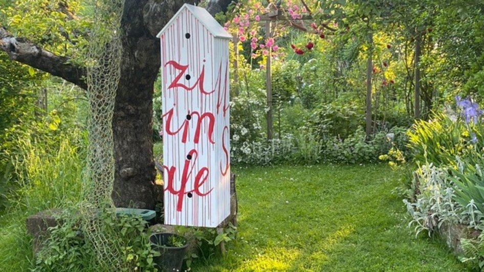 Ein farbenfrohes Schild im Garten mit dem Text 'zi um je'.