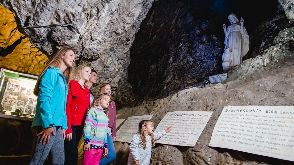 Familie erkundet die Lurgrotte Peggau mit einem Blick auf die Statue und Informationsschilder. | © TV Region Graz - Mias Photoart