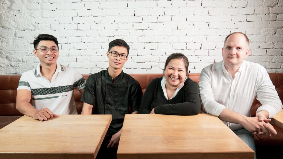 Vier Personen sitzen an einem Tisch in einem Restaurant mit Backsteinmauer. | © Ma Kitchen
