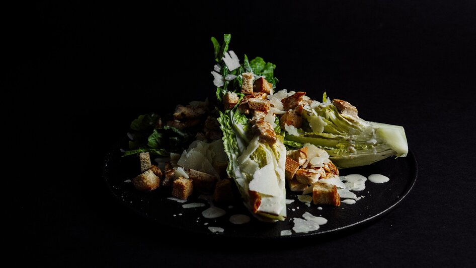 Frischer Cäsar-Salat mit Croutons und Parmesan auf schwarzem Hintergrund. | © Simona Donko