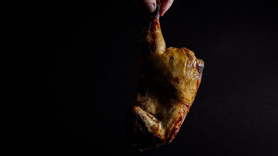 Gegrilltes Hähnchen wird über einer Platte mit Beilagen gehalten. | © Simona Donko