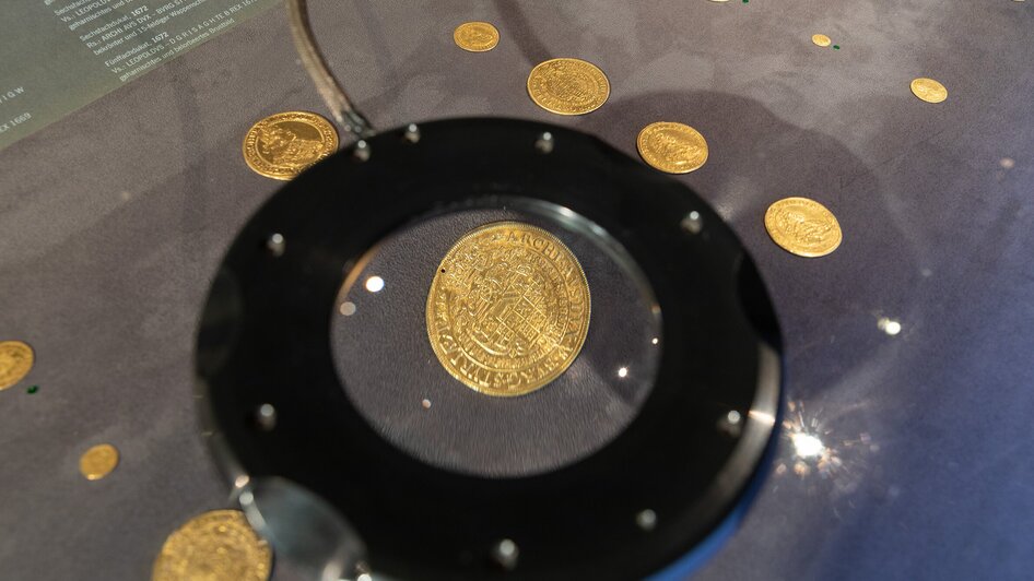 Goldene Münzen im Ausstellungsstück, beleuchtet von oben. | © Universalmuseum Joanneum - N. Lackner
